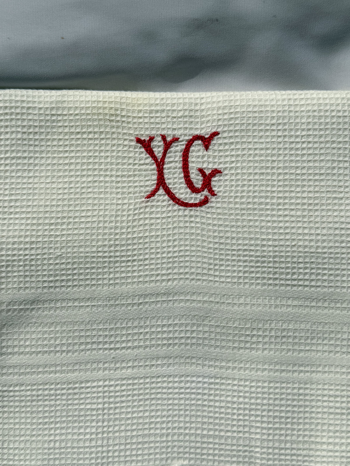 Bílá utěrka s červeným monogramem a třásněmi